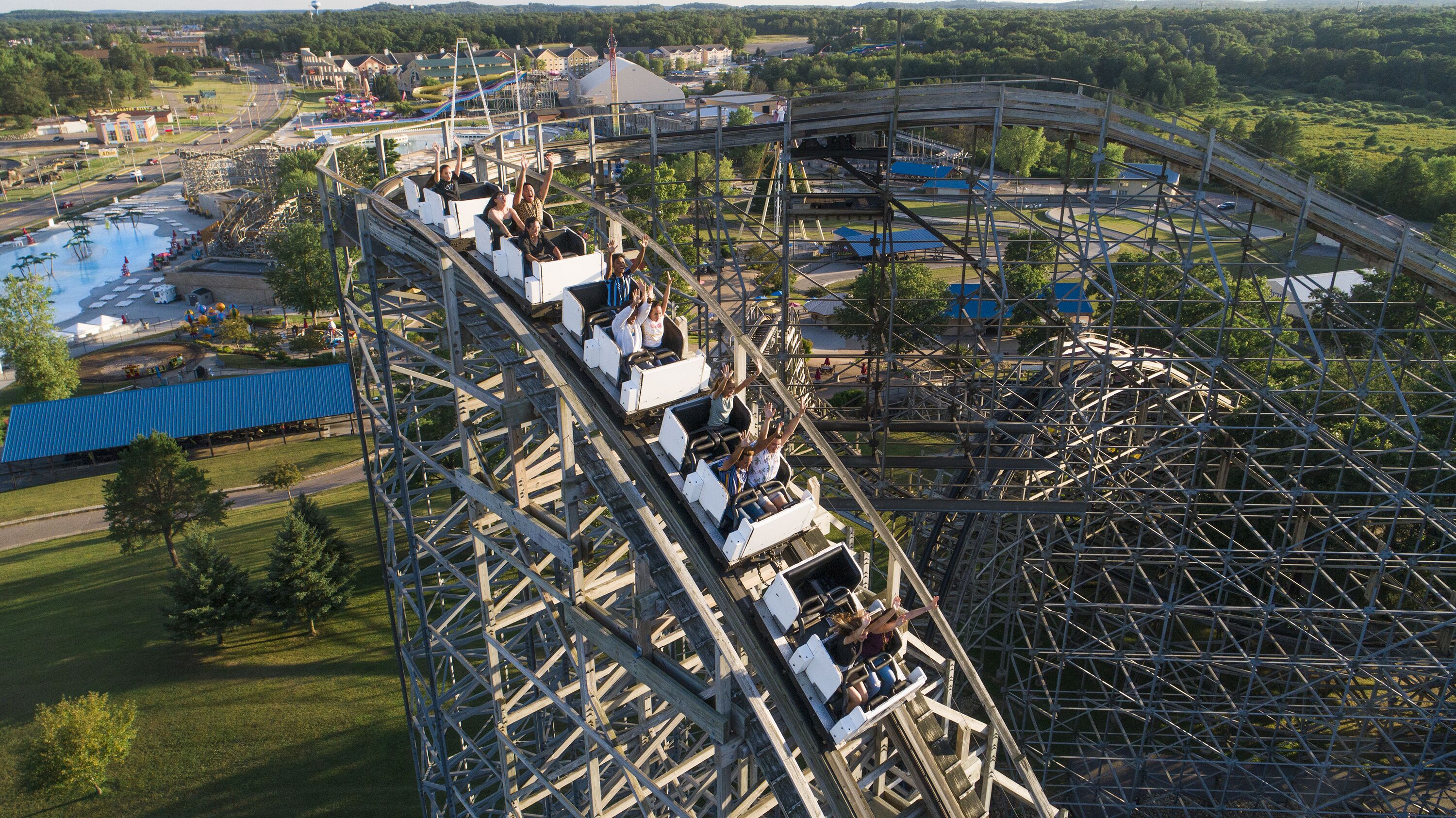 A roller coaster with passengers, surrounded by a park with various structures and greenery.
