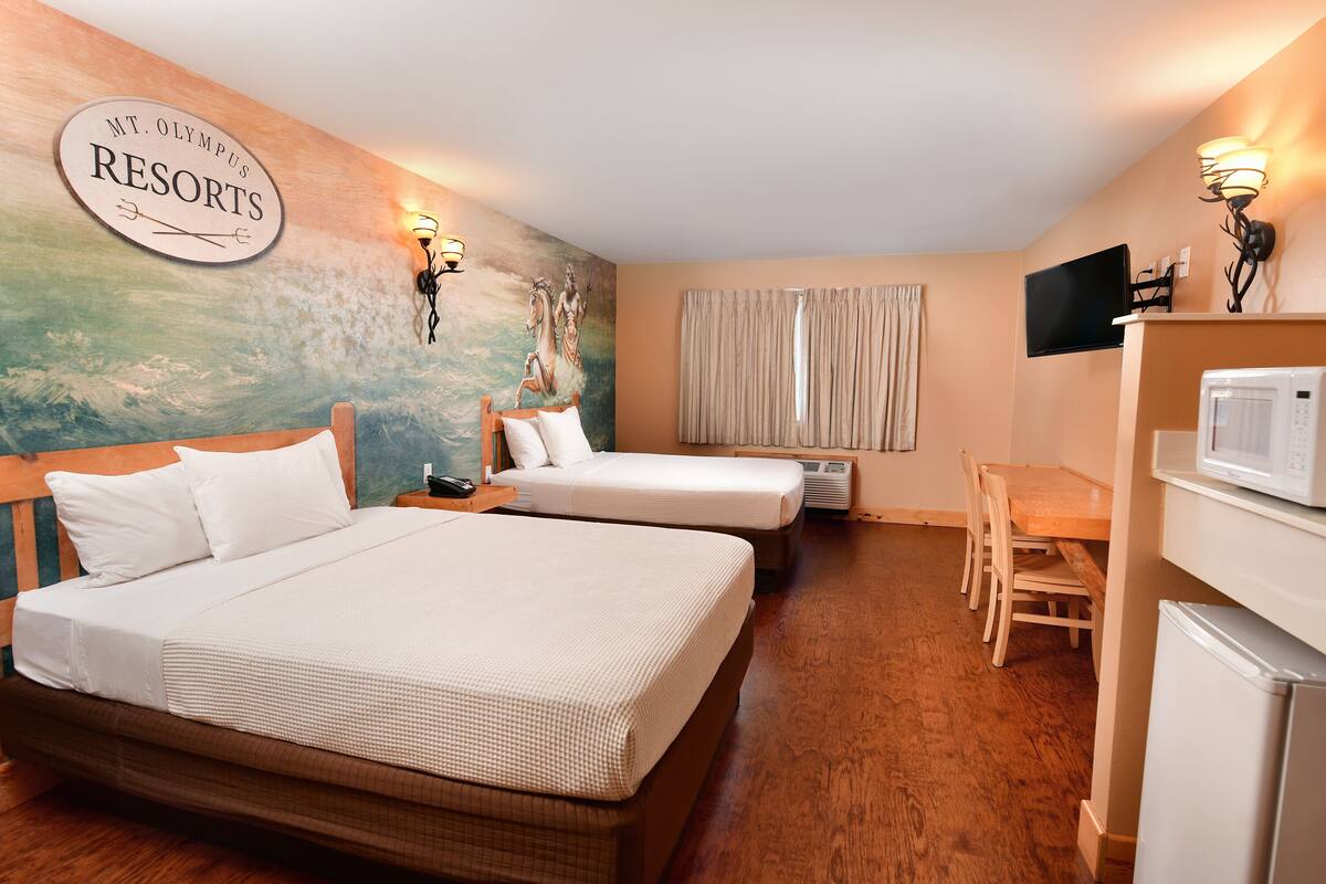 A hotel room with two beds, a dining table, a TV, and a sign reading "Mt. Olympus Resorts".