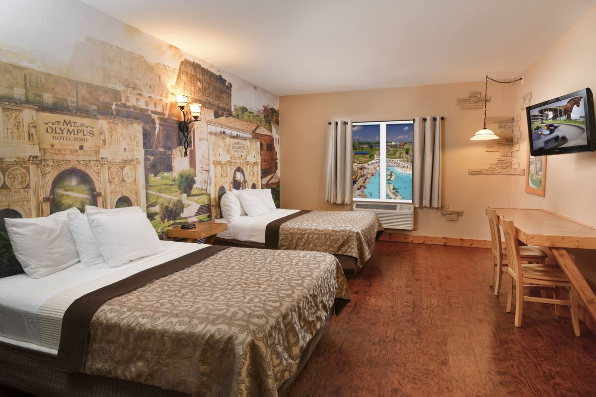 A hotel room with two beds, a wooden desk, a TV, and a view of a pool through a window.