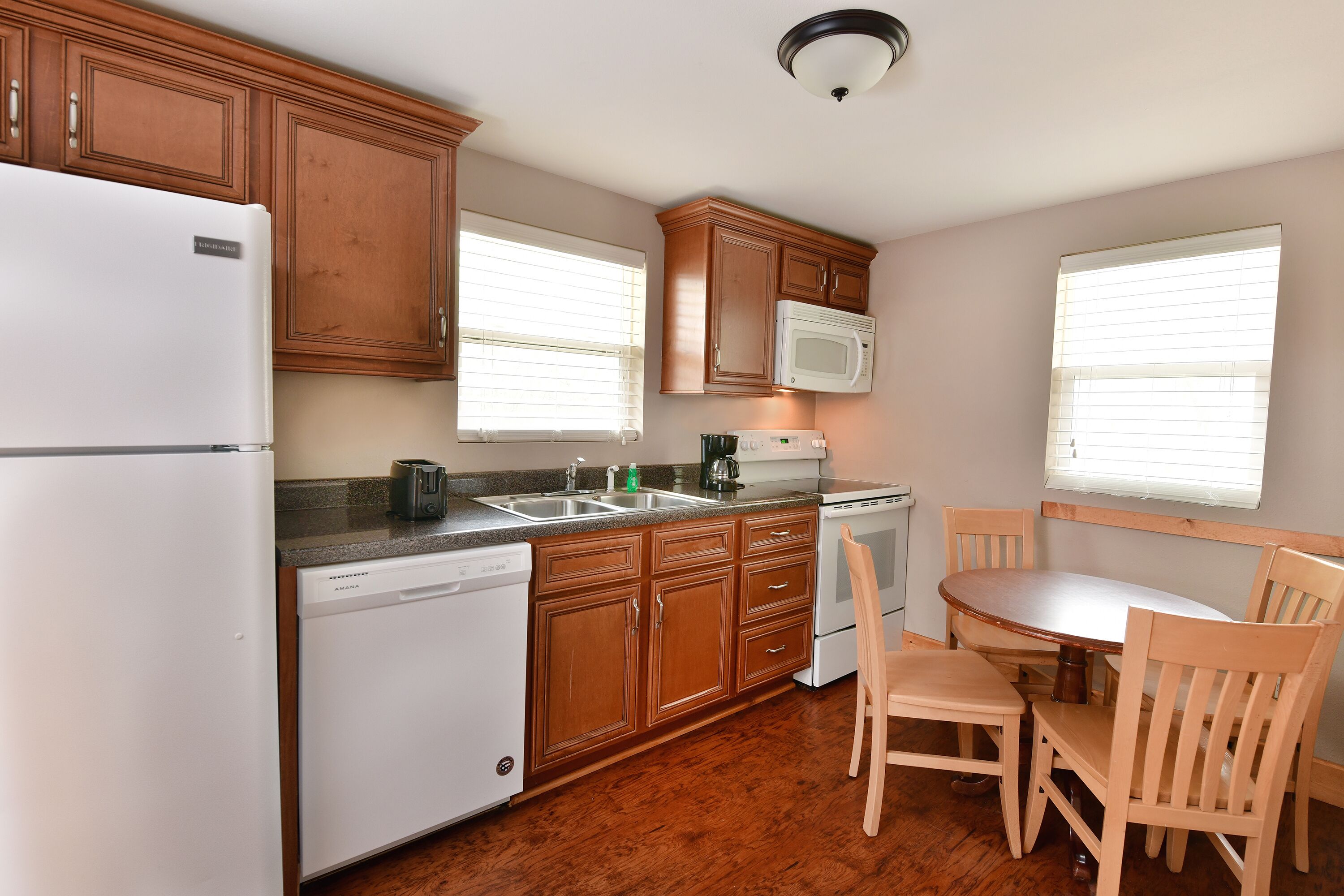 Una cocina con armarios de madera, un refrigerador blanco, un microondas, un lavavajillas y una mesa de comedor con sillas.