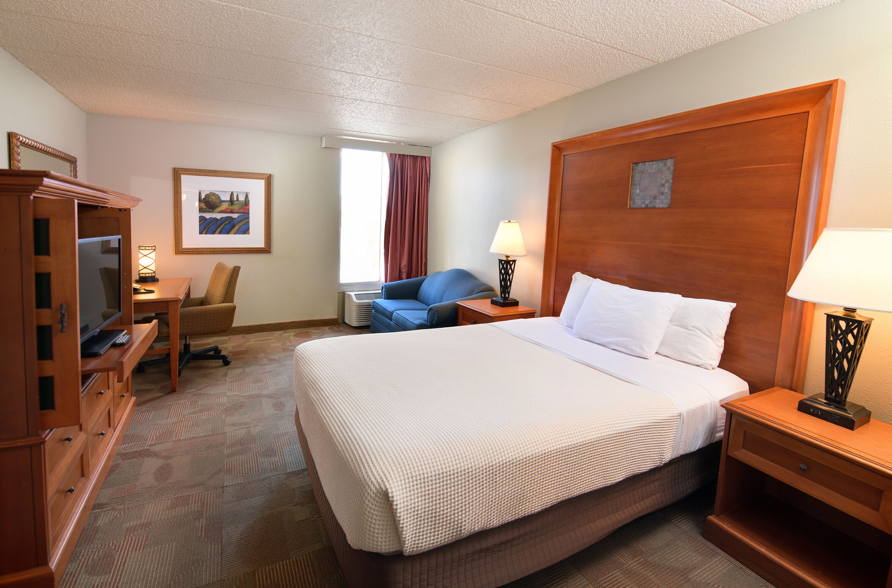 Ein Hotelzimmer mit einem großen Bett, einem Schreibtisch, einem Sessel, einem Fernseher und einer Lampe.