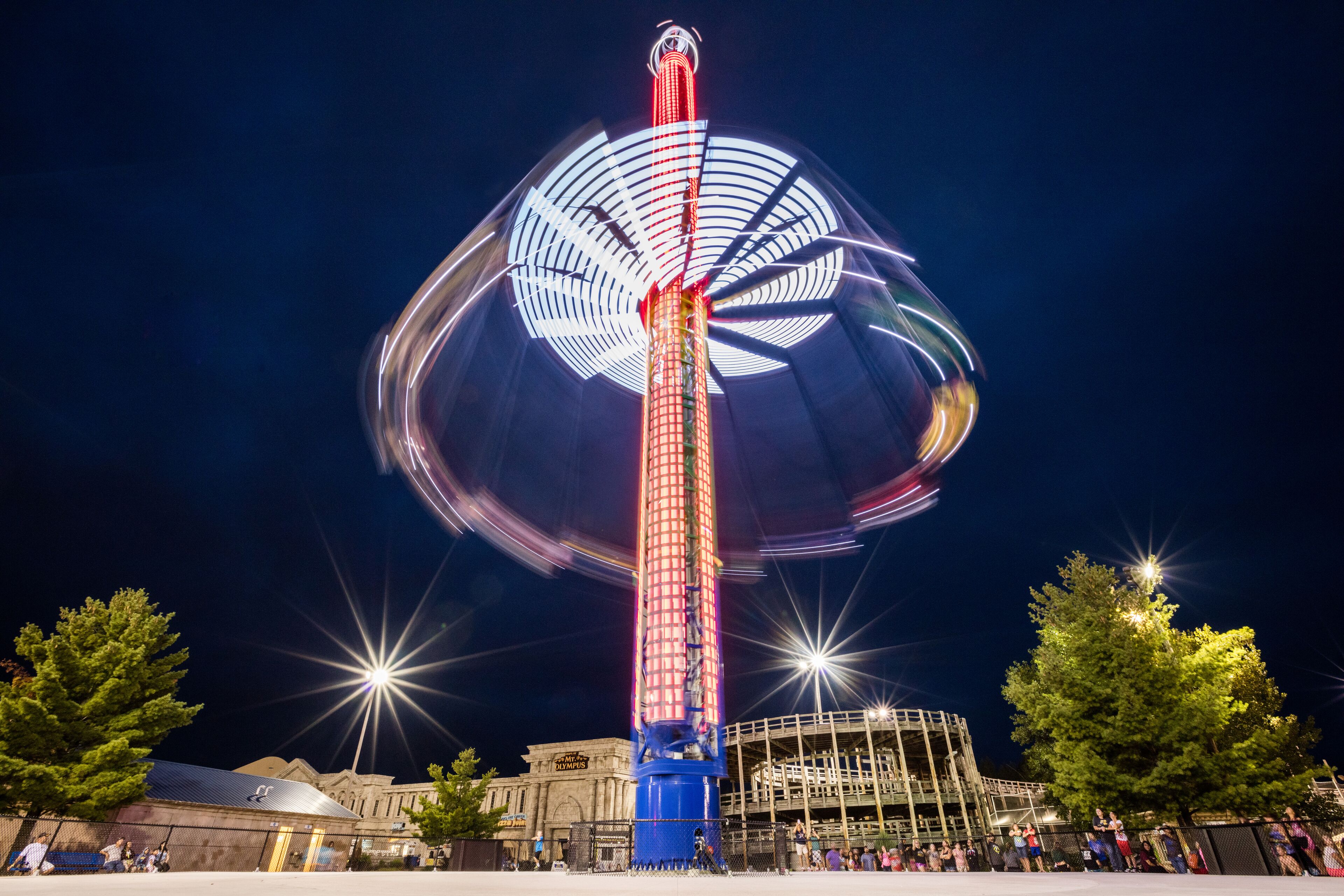 A Ferris wheel with a red and white design, surrounded by trees and a building in the background.