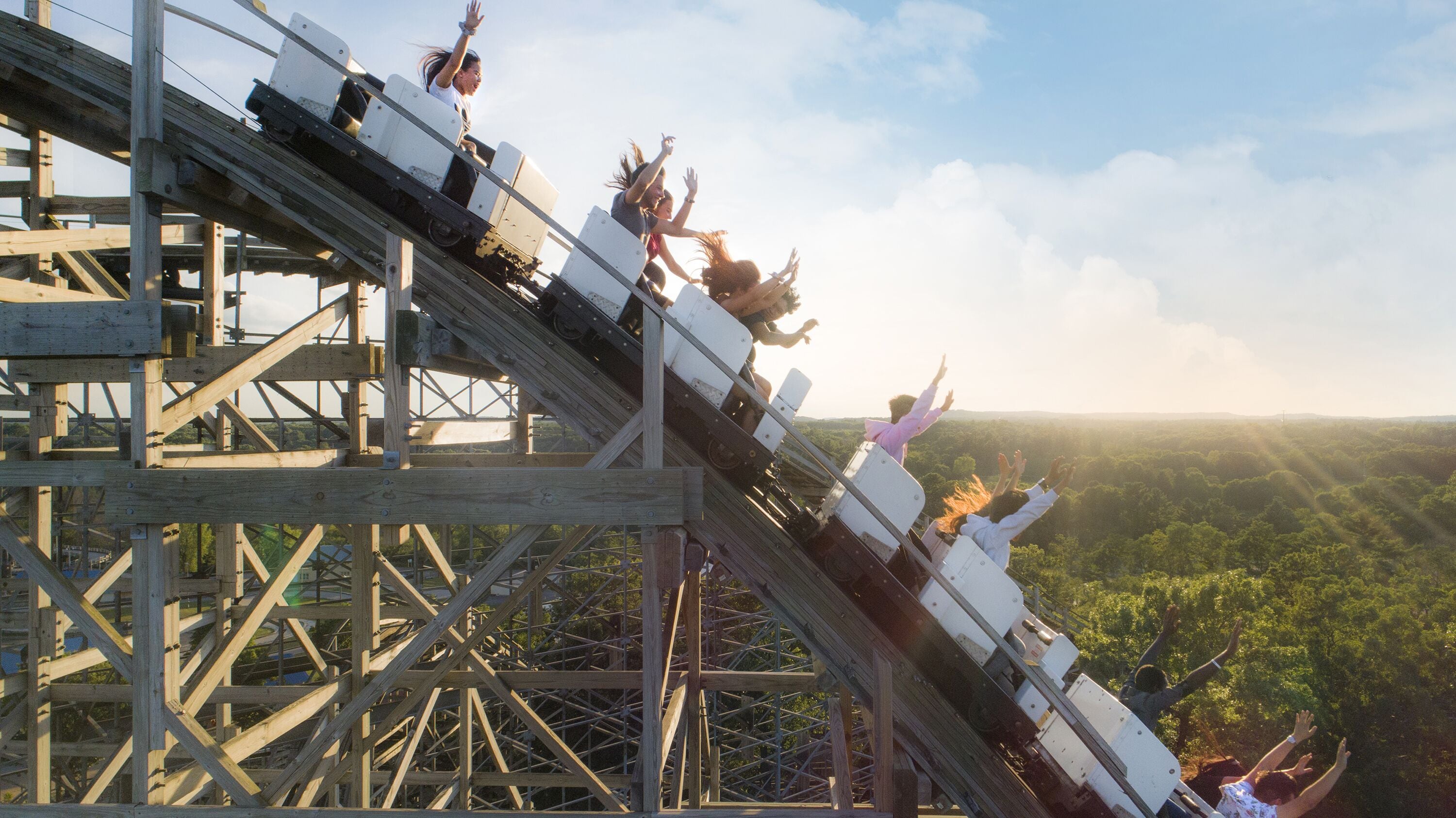 A wooden roller coaster with a steep incline and a view of a forested landscape in the background.