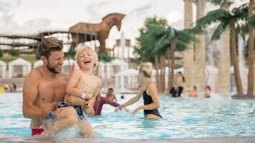 A man and a child in a swimming pool with palm trees and a horse statue in the background.