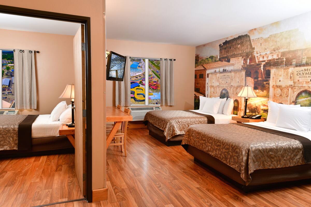 A hotel room with two beds, a desk, a chair, a TV, and a mural of a historical building.