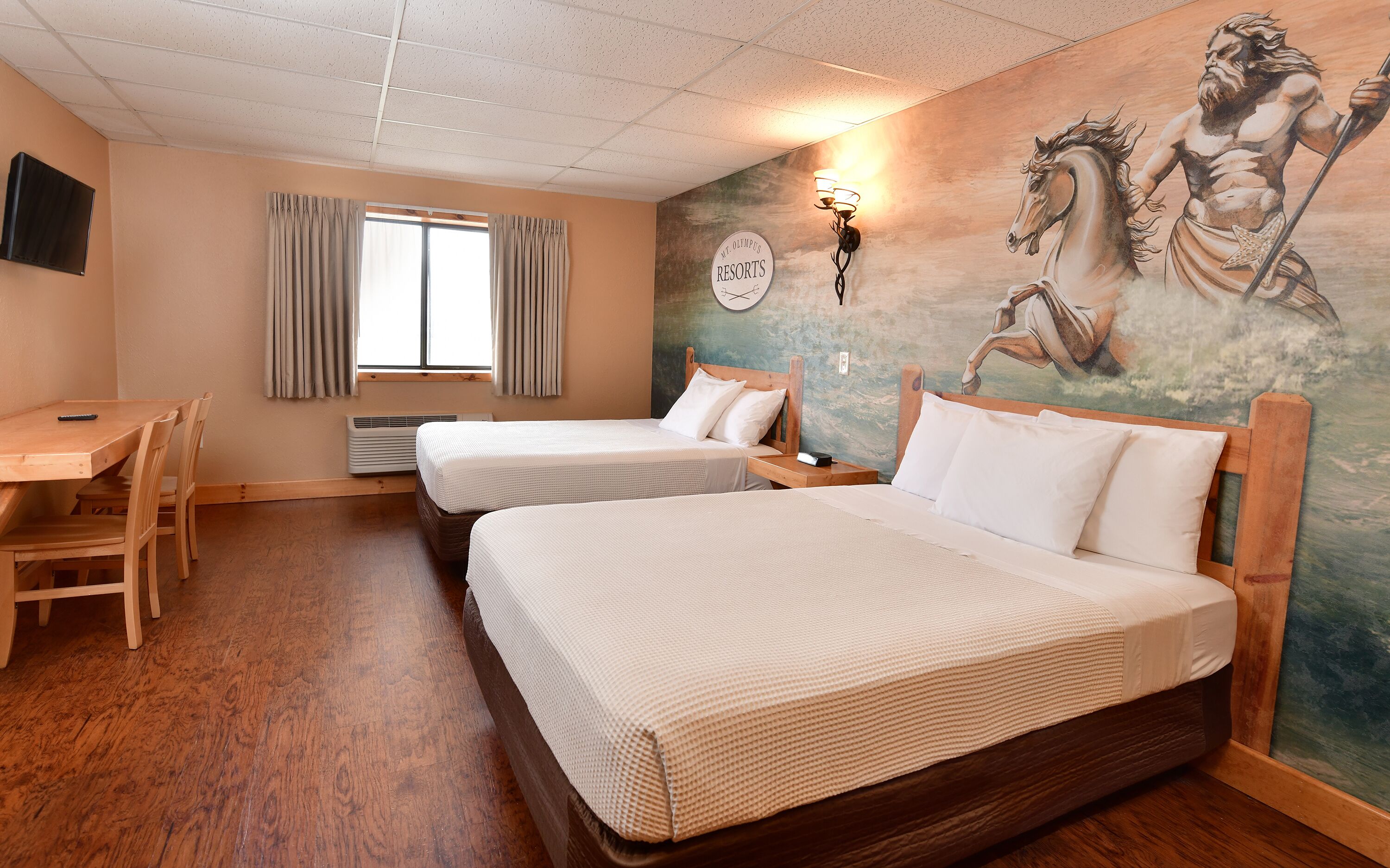 A hotel room with two beds, a desk, a TV, and a mural.
