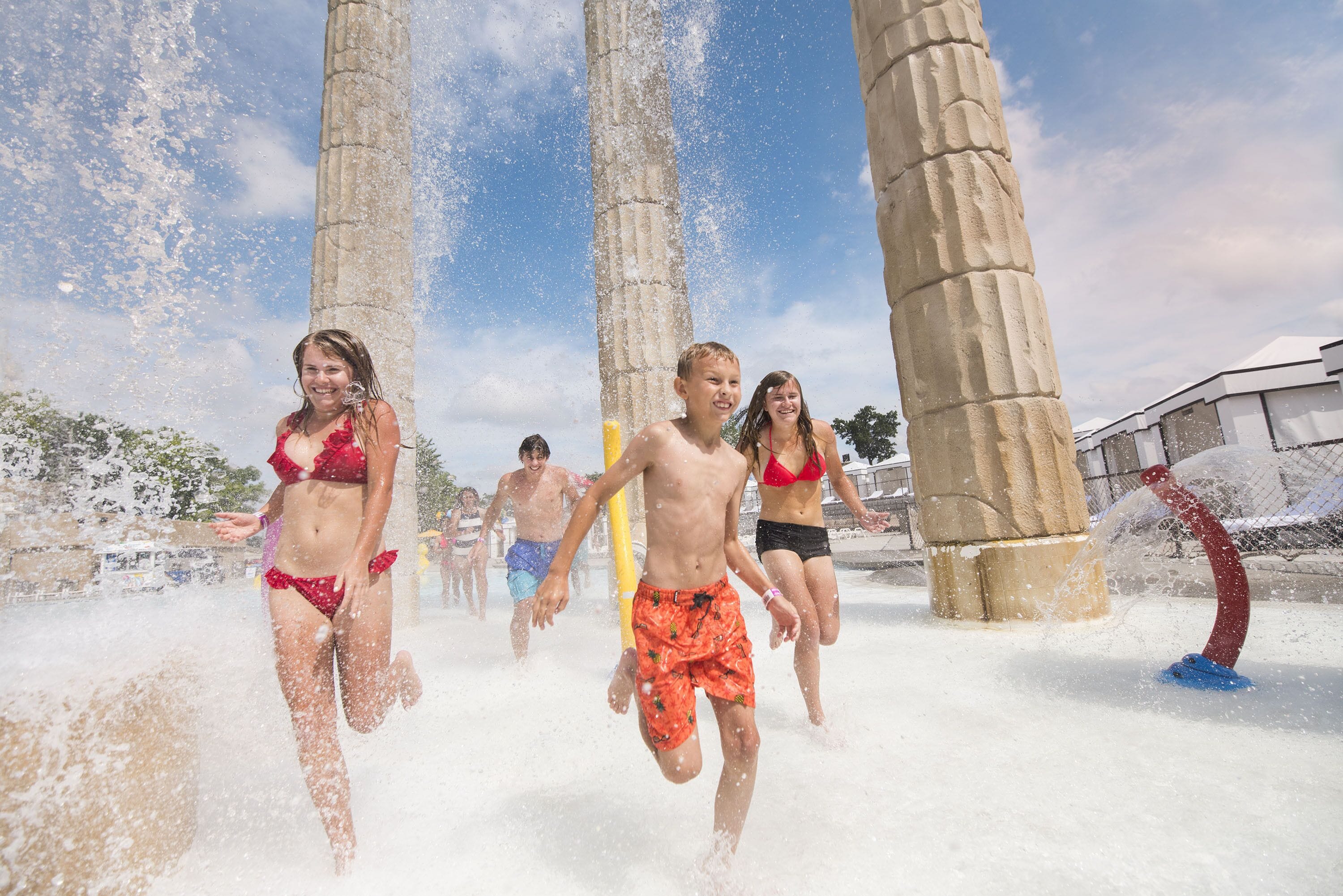 A group of people playing in a water fountain area with stone columns.