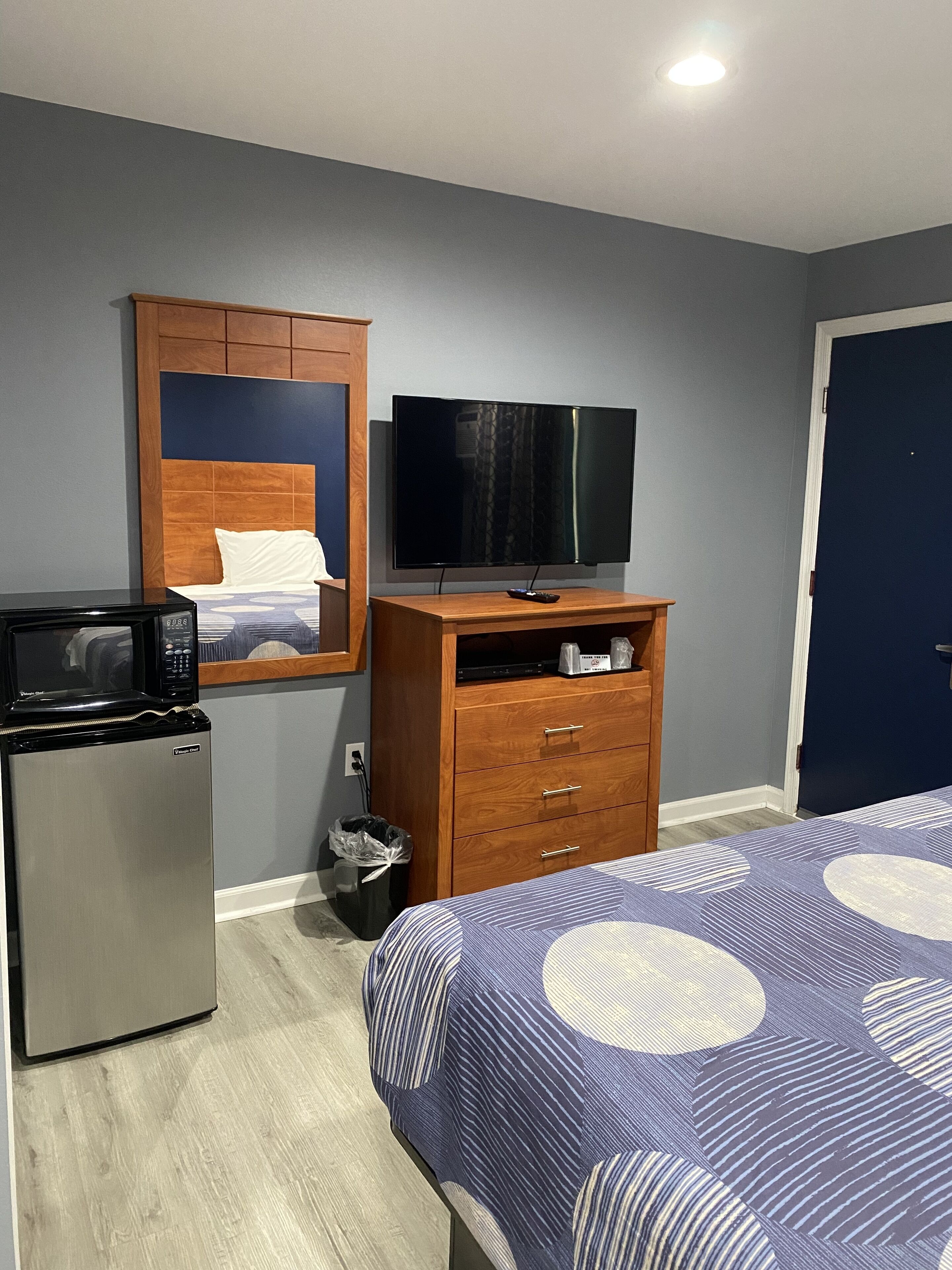 Habitación de hotel con cama, cómoda de madera, televisor, microondas y refrigerador pequeño.