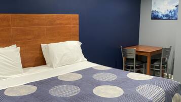 Habitación de hotel con cama, cabecero de madera, mesa de comedor con sillas y un cuadro en la pared.