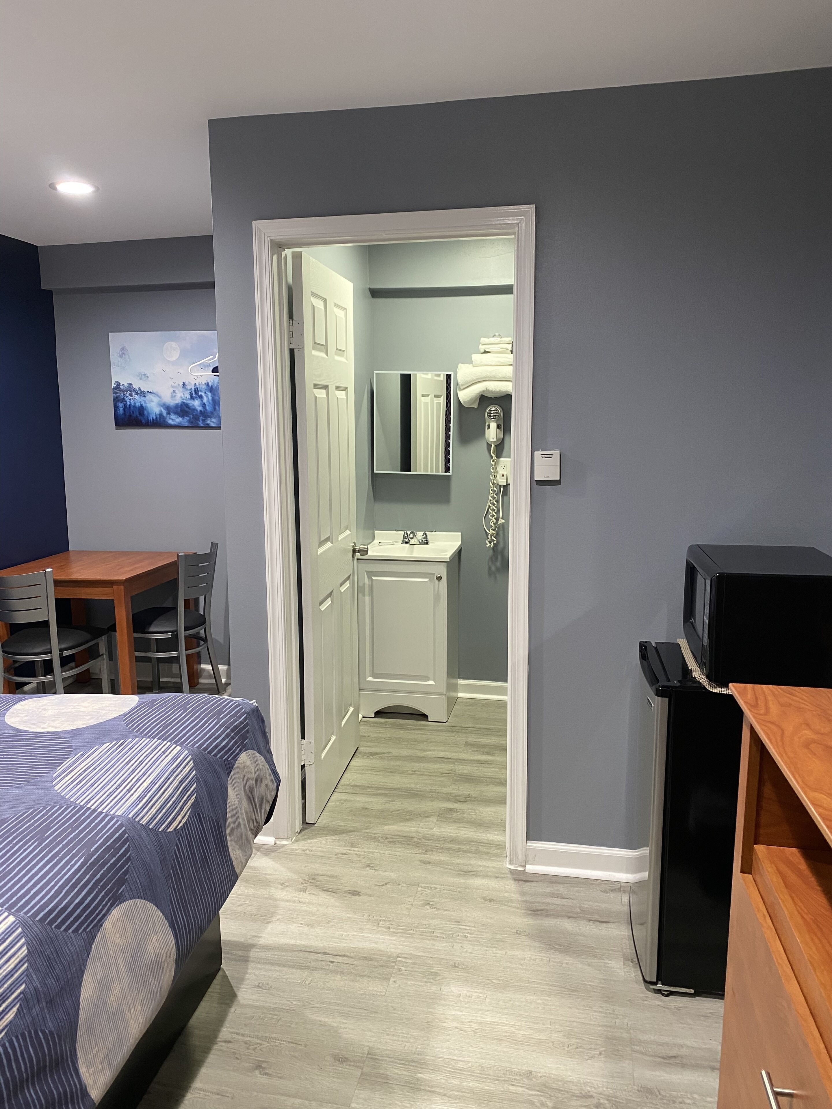 Un dormitorio con cama, escritorio y televisor. Se ve un baño a través de una puerta abierta.