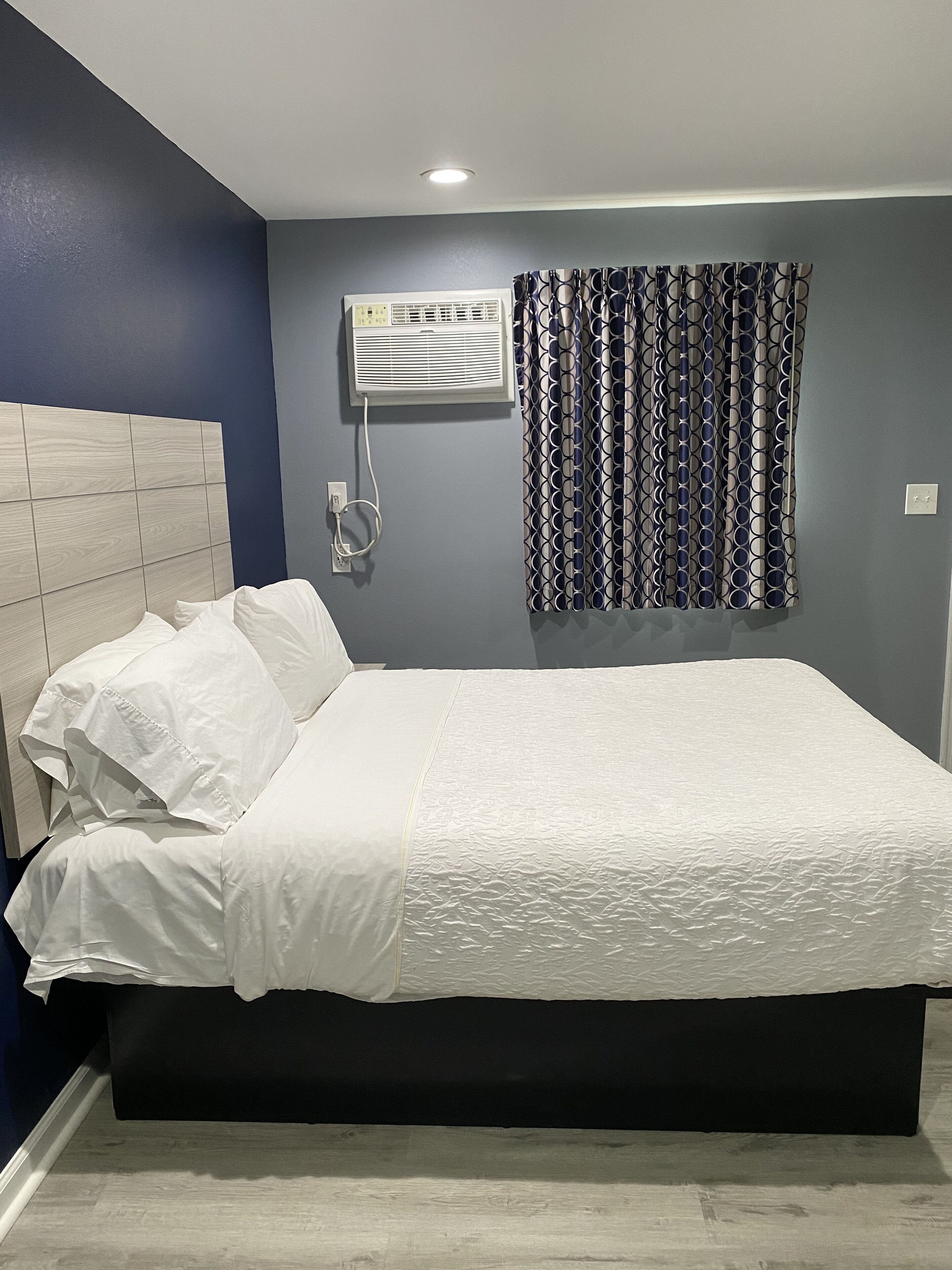 Un dormitorio moderno con una cama grande, cabecera, aire acondicionado de pared y cortina estampada.