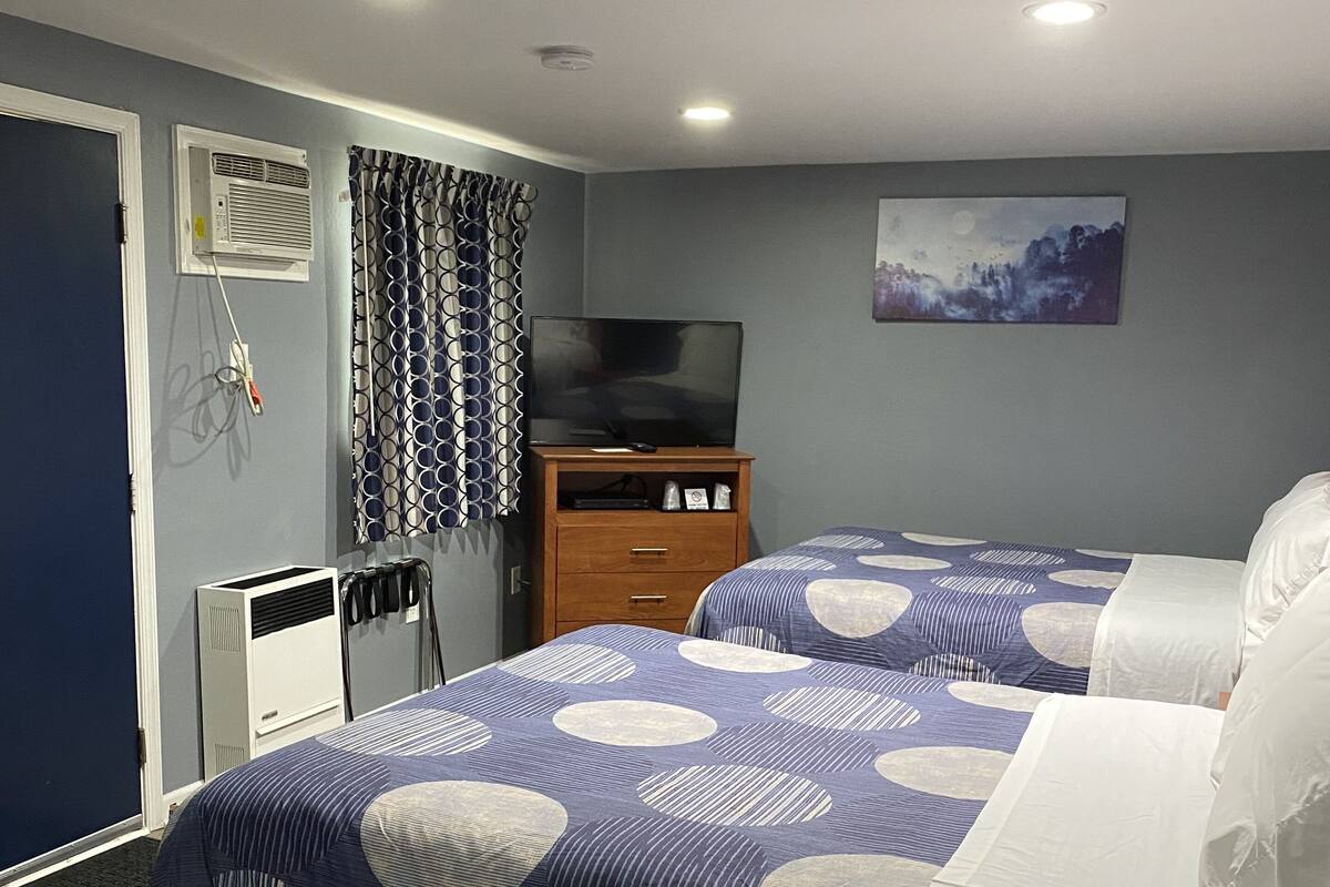A hotel room with two beds, a TV, a painting, and a window with curtains.