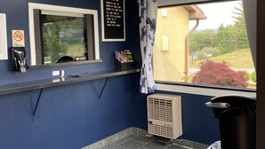 Ein Hotel-Empfangsbereich mit blauer Wand, einer Rezeption, einem Rauchverbotsschild, einem Fenster mit Blick auf Grünflächen und einem Schild mit Eincheckzeiten und Regeln.