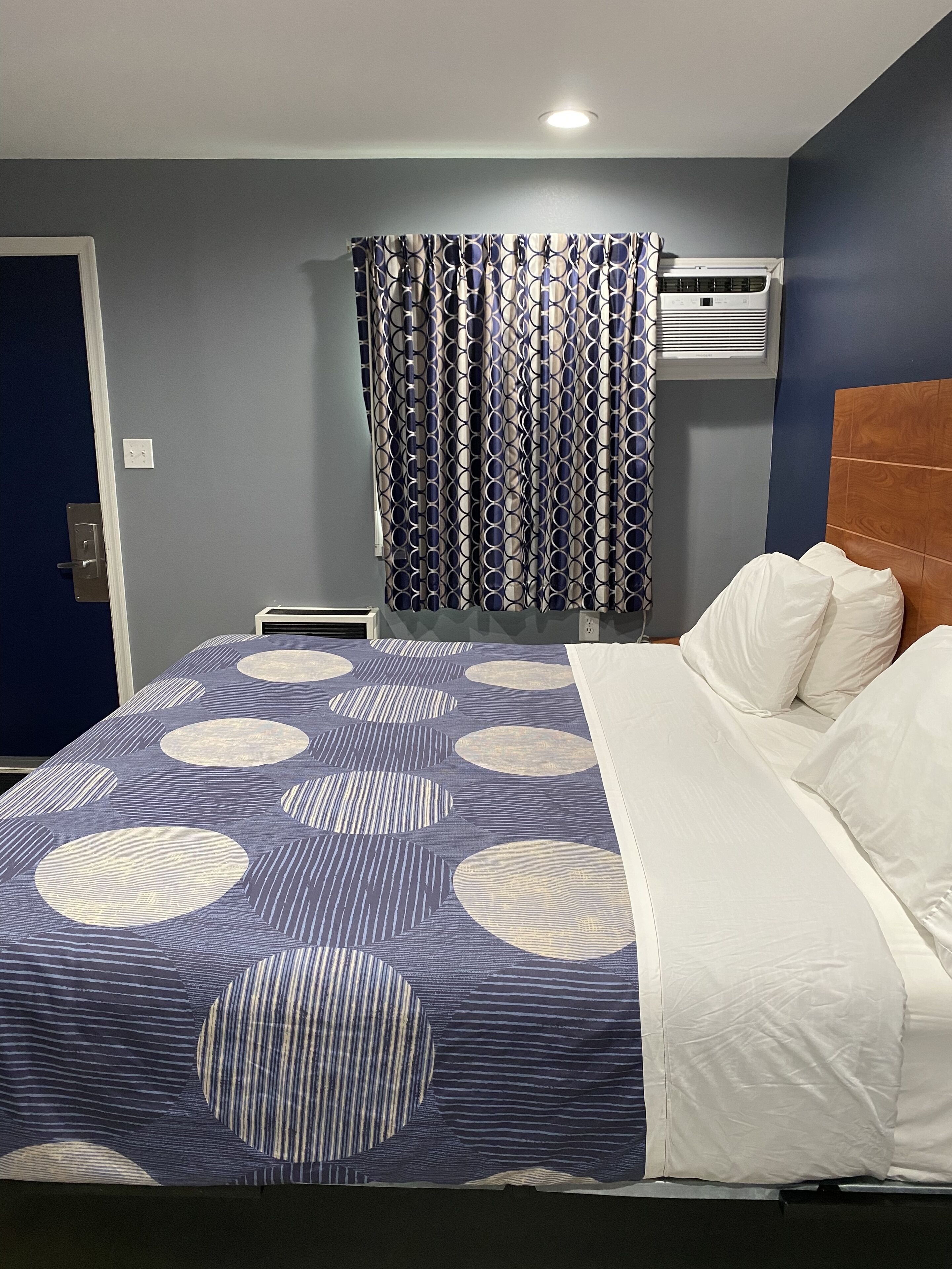 Ein Hotelzimmer mit Bett, einem Vorhangfenster, einer Klimaanlage und einer Wandleuchte.