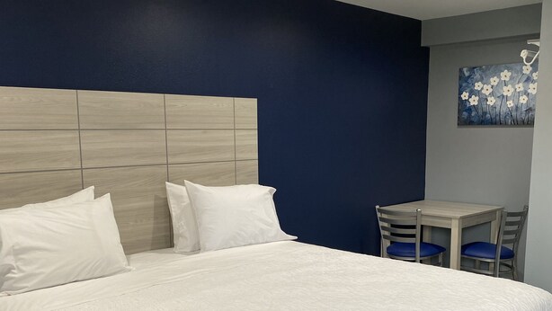 Ein großes Bett mit hölzernem Kopfteil, weißer Bettwäsche und einem kleinen Tisch mit Stühlen in einem Zimmer mit dunkelblauen Wänden und eingelassenen Deckenleuchten.