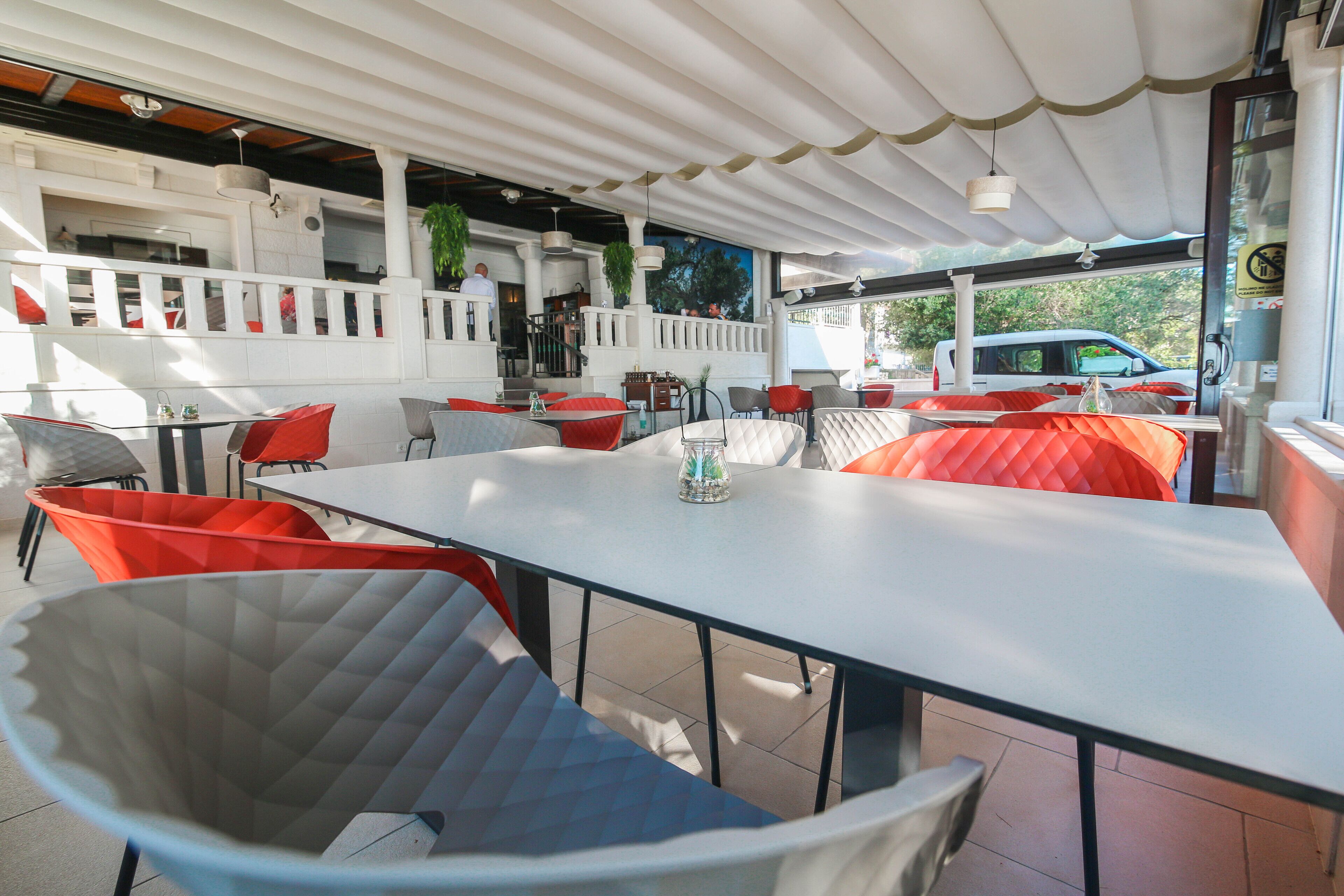 An outdoor dining area with tables and chairs, a covered seating area, and a view of a vehicle outside.