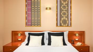 Quarto de hotel com uma cama grande, duas mesas de cabeceira e uma luminária fixada na parede.