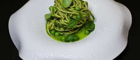 A white plate with a pasta dish, garnished with green sauce and basil leaves.