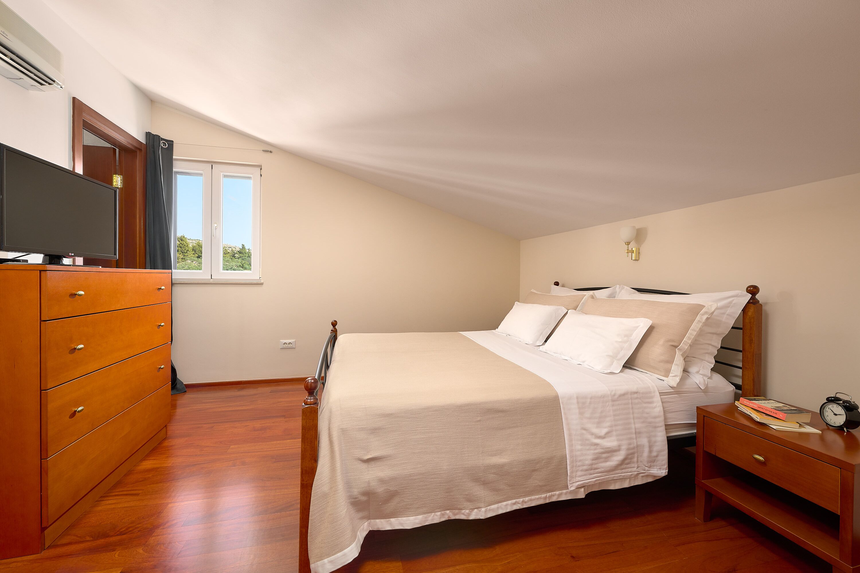 A bedroom with a bed, dresser, nightstand, and a TV on the dresser.