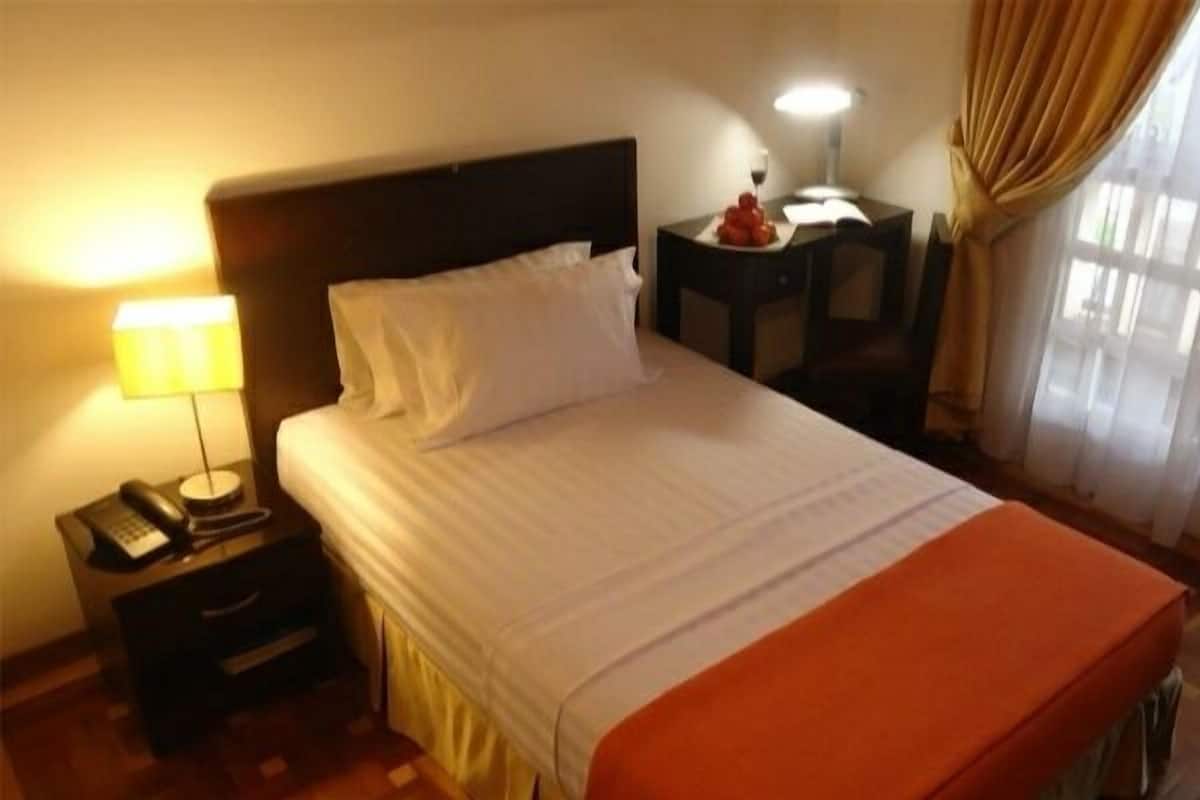 A hotel room with a bed, a bedside lamp, a telephone, a nightstand, and a window with curtains.