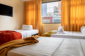 A hotel room with two beds, a window with curtains, and a view of buildings outside. - Casa Coliving Day 121  (Bogotá)