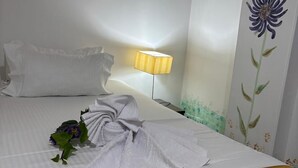 A neatly made bed with a white comforter and pillows, a bedside lamp, and a wall with a floral mural. - Casa Coliving Day 121  (Bogotá)