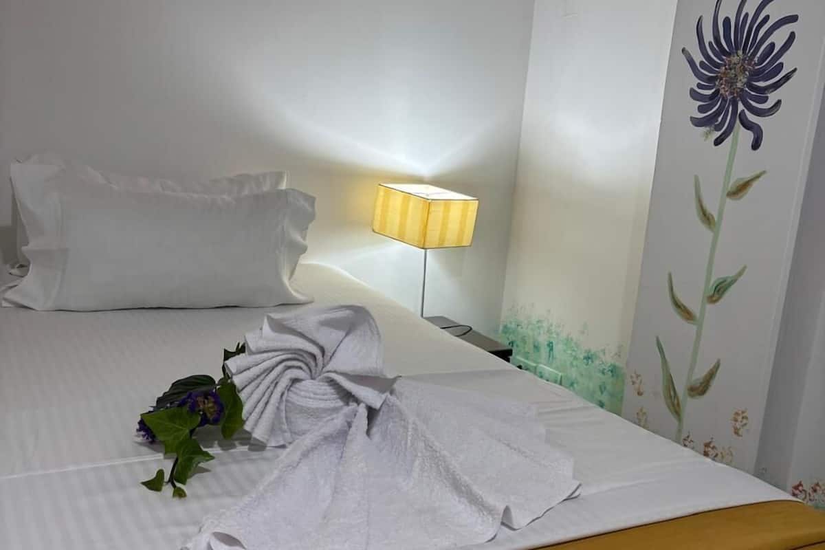 A neatly made bed with a white comforter and pillows, a bedside lamp, and a wall with a floral mural.