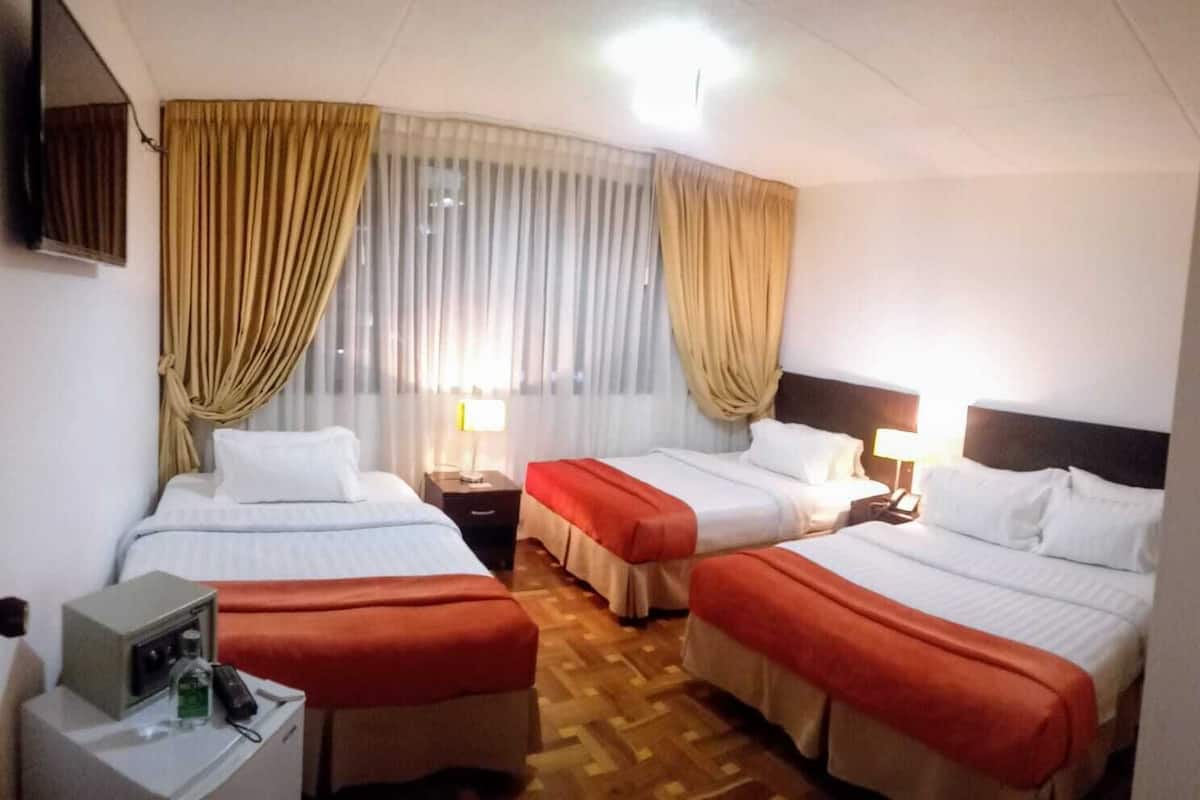 A hotel room with two beds, a desk with a lamp, and a TV on the wall.