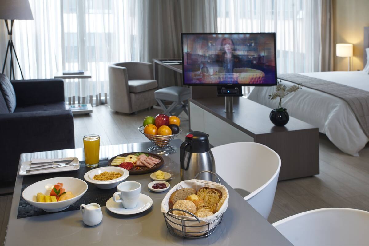 Habitación de hotel con una mesa de comedor preparada para el desayuno, un televisor y una cama.