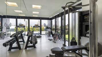 A modern gym with various exercise equipment, large windows, and a view of the city.