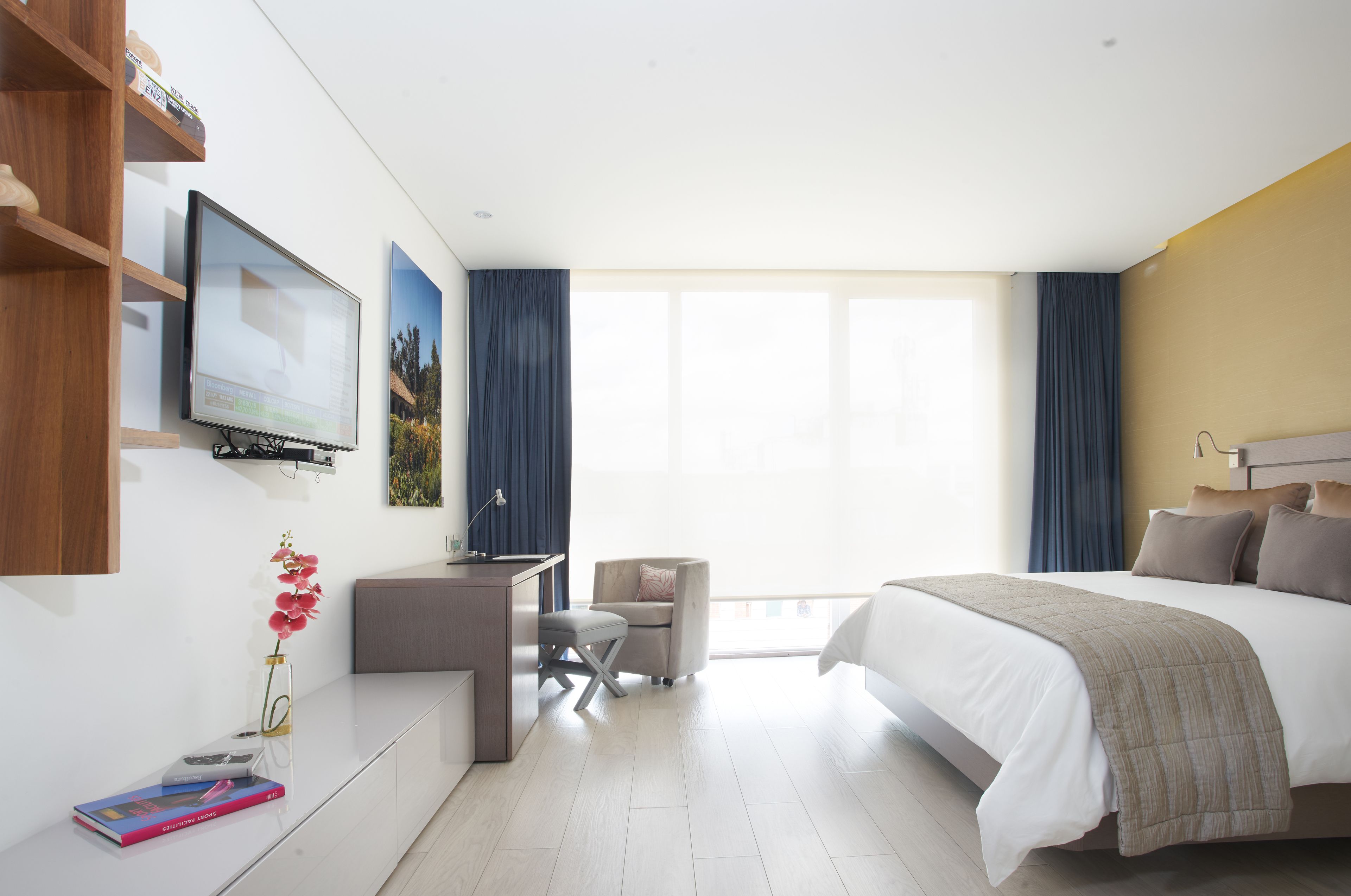 Ein modernes Hotelzimmer mit einem großen Bett, einem Schreibtisch mit Stuhl, einem an der Wand befestigten Fernseher und einem Fenster mit Vorhängen.