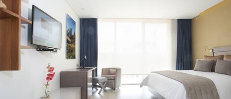 Ein modernes Hotelzimmer mit einem großen Bett, einem Schreibtisch mit Stuhl, einem an der Wand befestigten Fernseher und einem Fenster mit Vorhängen.