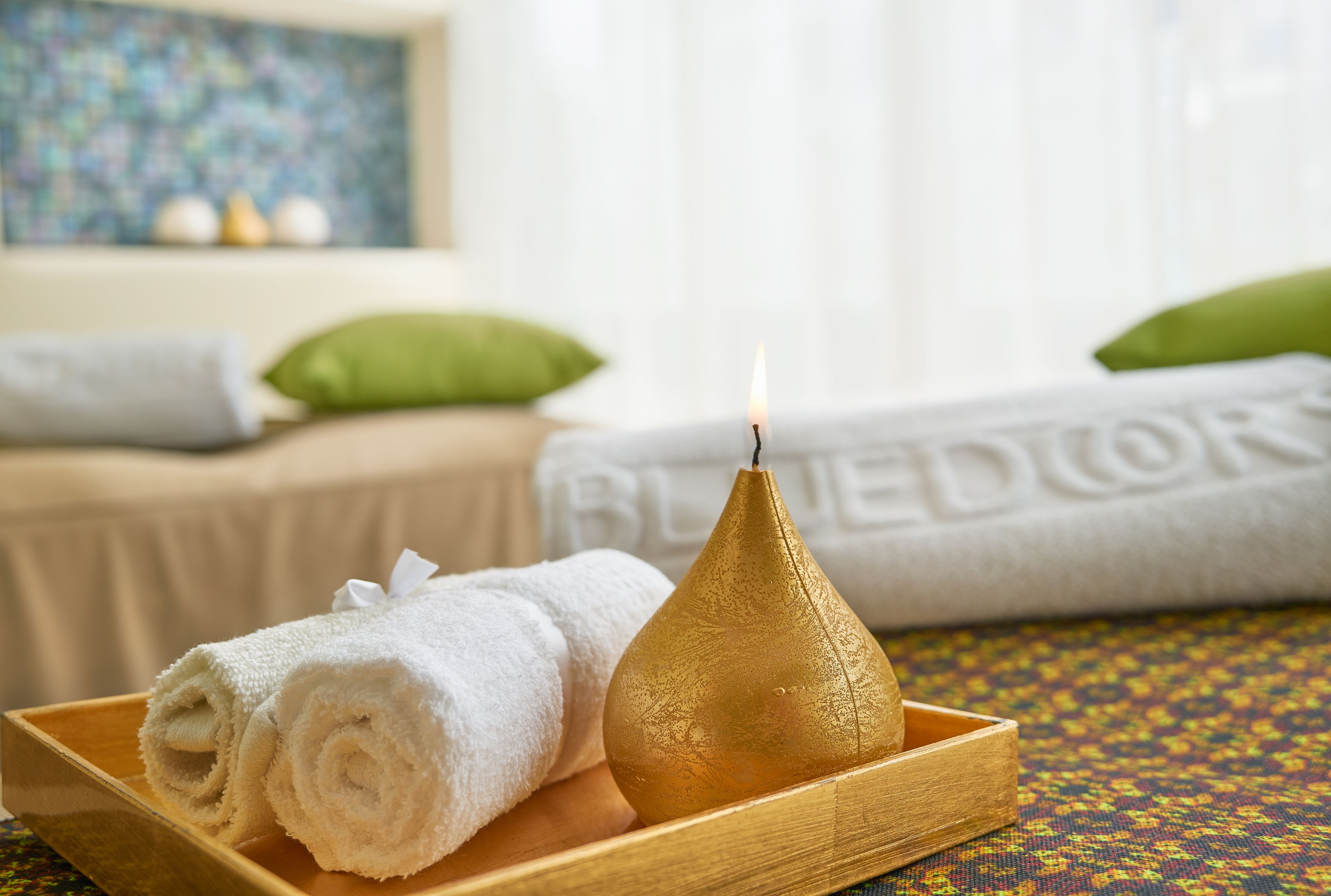 A wooden tray with rolled white towels and a lit candle.