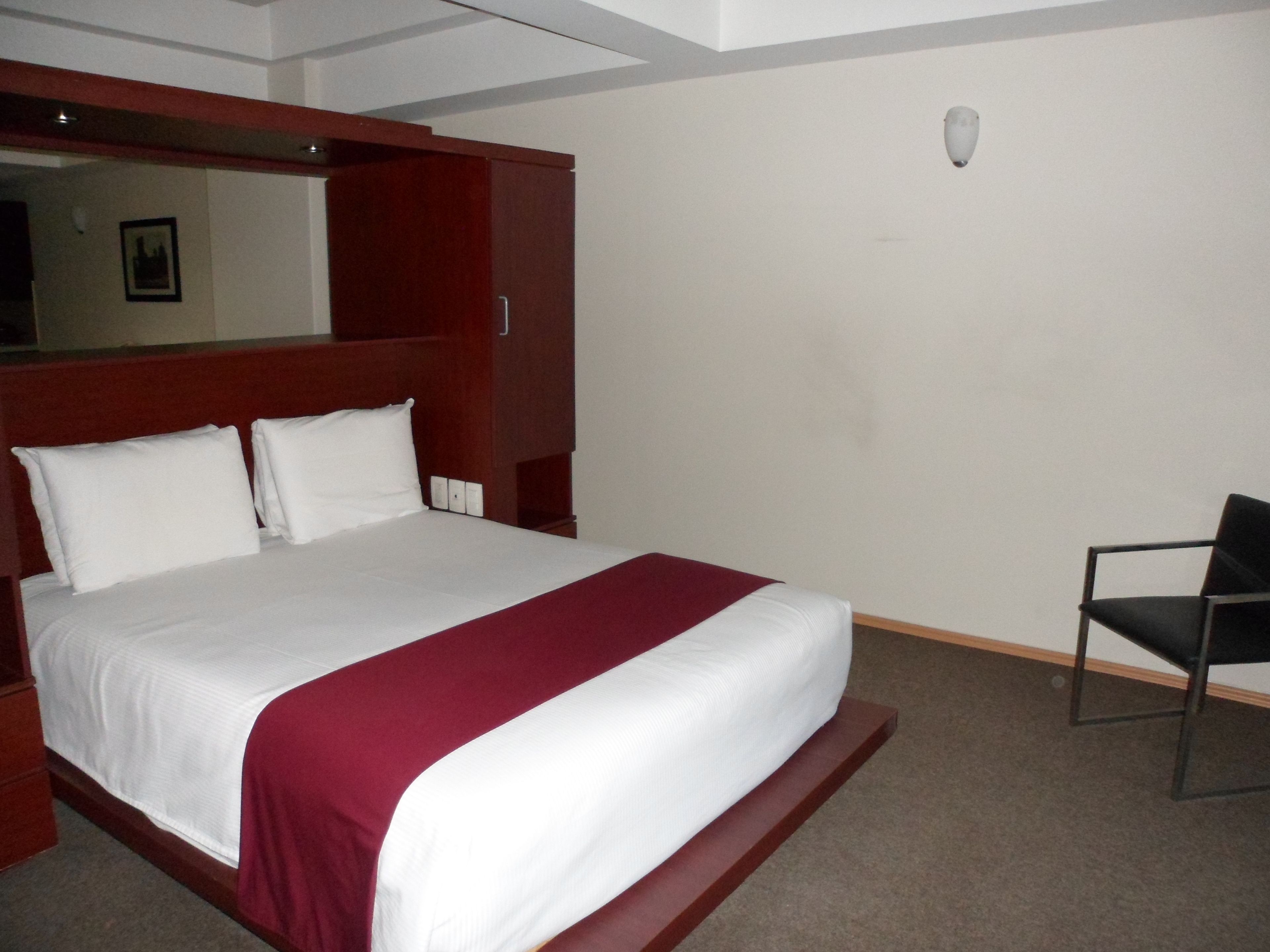 A hotel room with a large bed, a wooden headboard, a chair, and a small table.