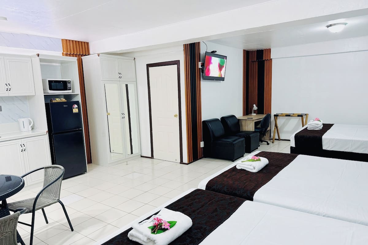 A hotel room with a bed, a desk, a chair, a TV, and a kitchenette.