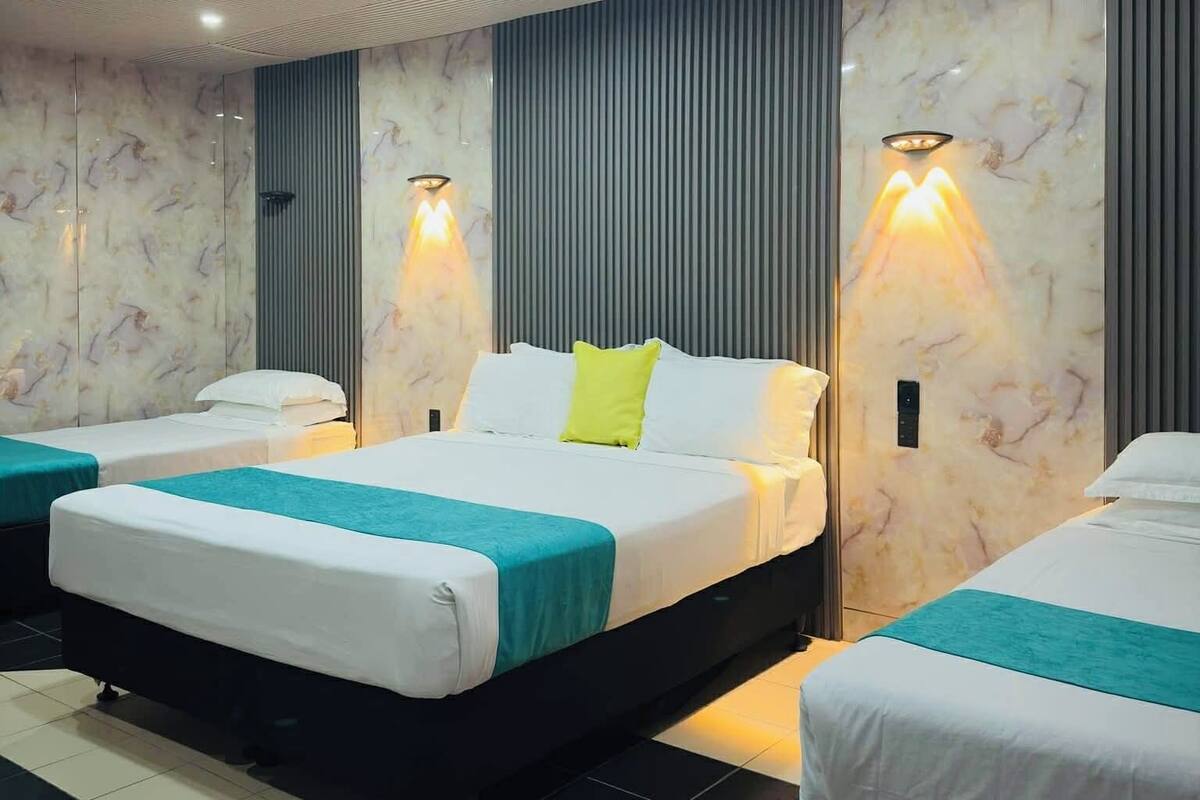 A hotel room with a large bed, two smaller beds, a tiled floor, and a ceiling with recessed lighting.