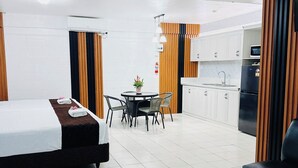 A modern hotel room with a bed, a small dining table with chairs, a kitchen area with a refrigerator, and a bathroom with a shower. - Moatoga Hotel (Apia)