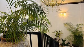 A hallway with a large potted plant, a black railing, a mosaic floor, and a chandelier. - Moatoga Hotel (Apia)