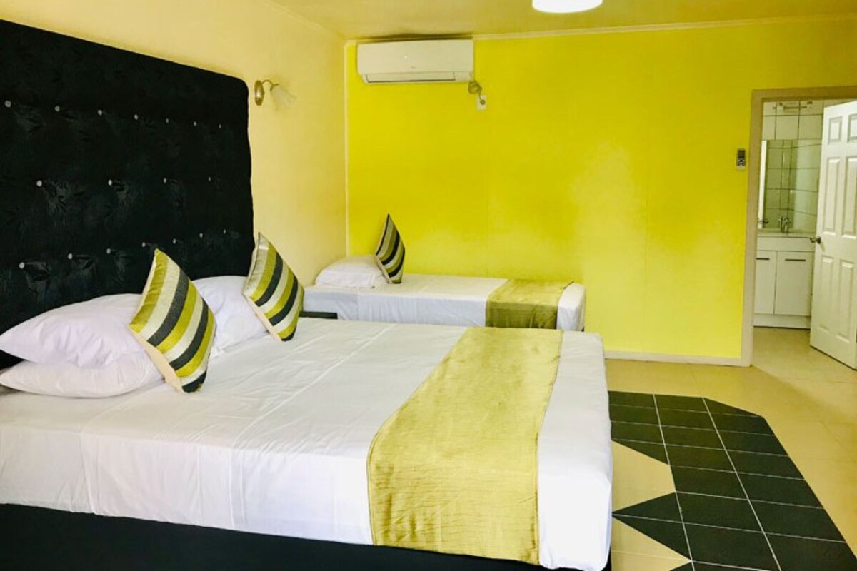 A hotel room with two beds, a black headboard, a yellow wall, and a tiled floor.