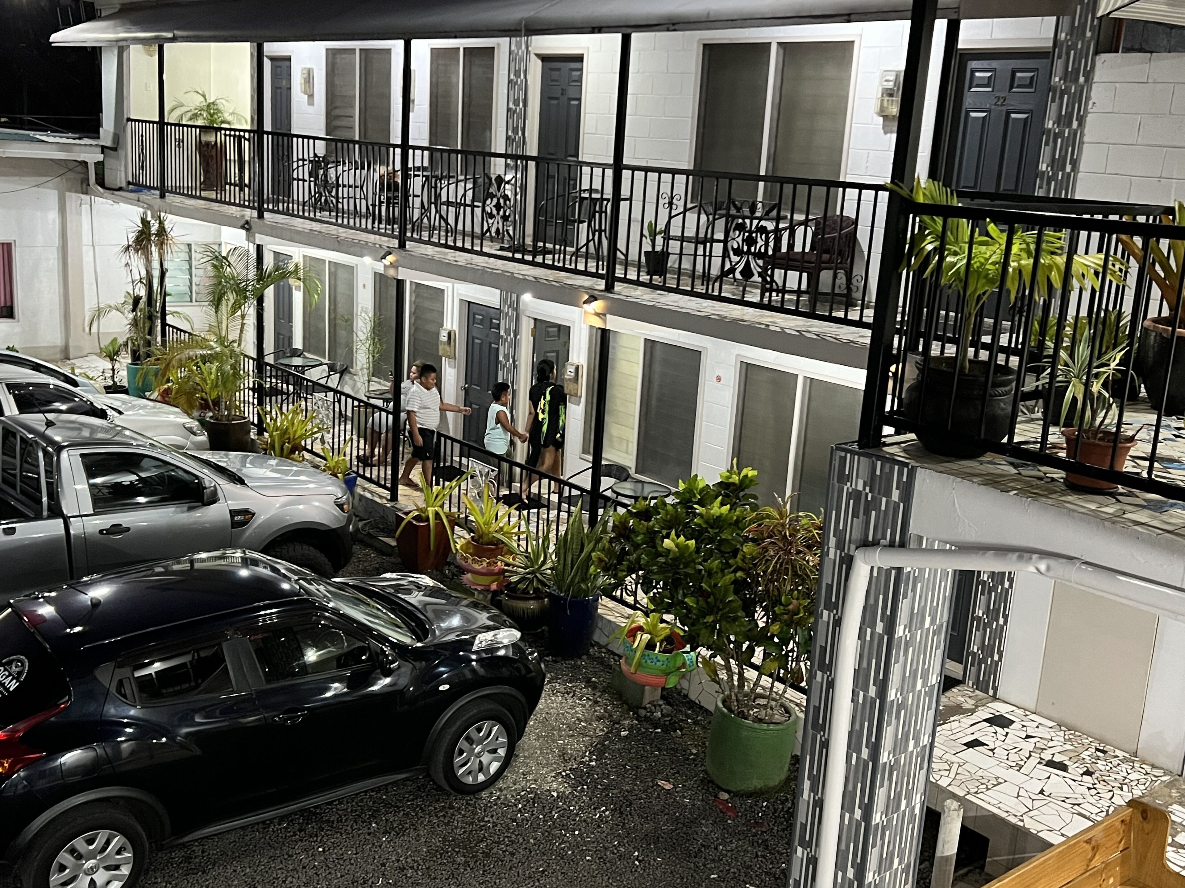 A multi-story building with a balcony, potted plants, and parked cars.