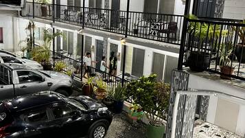 Un edificio de varios pisos con balcón, plantas en macetas y coches aparcados.