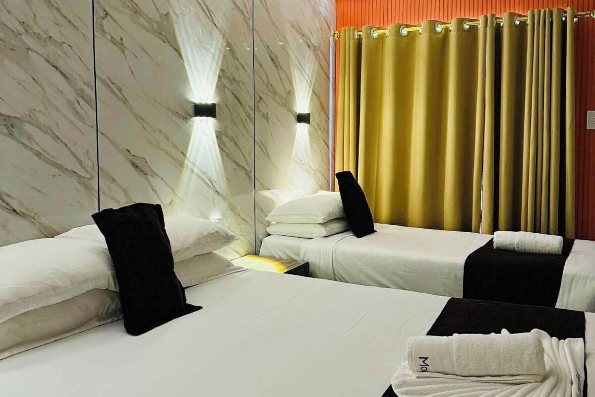 A hotel room with two beds, marble walls, a ceiling light, and a curtain.
