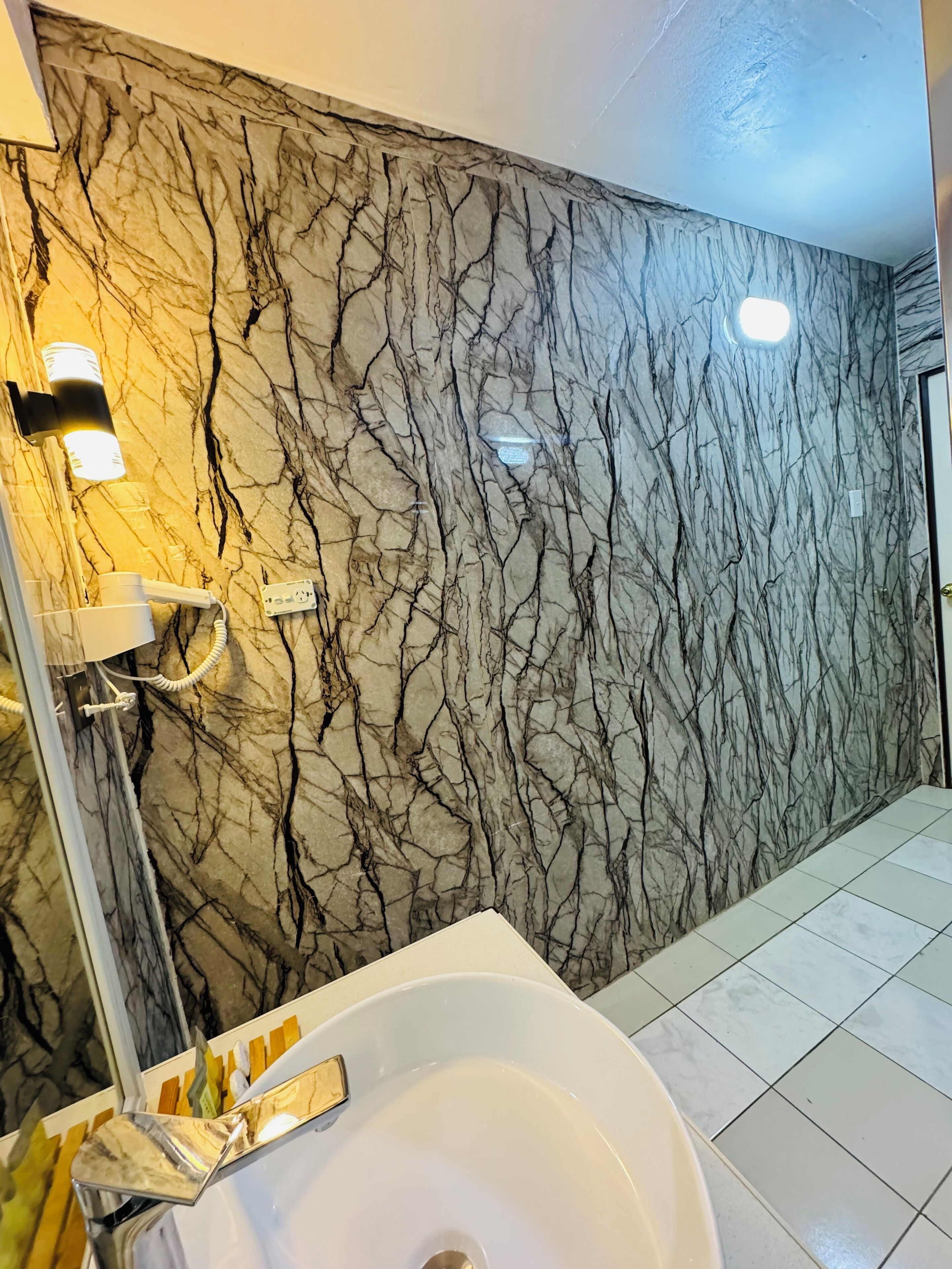 Un baño con pared de mármol, un lavabo blanco y un espejo.