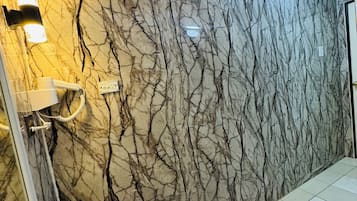 Een badkamer met een marmeren wand, een witte wastafel en een spiegel.