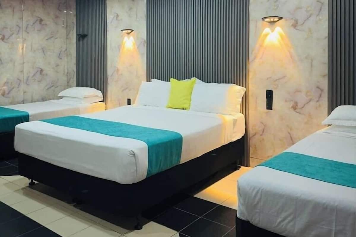 A hotel room with a large bed, two smaller beds, a tiled floor, and a ceiling with recessed lighting.