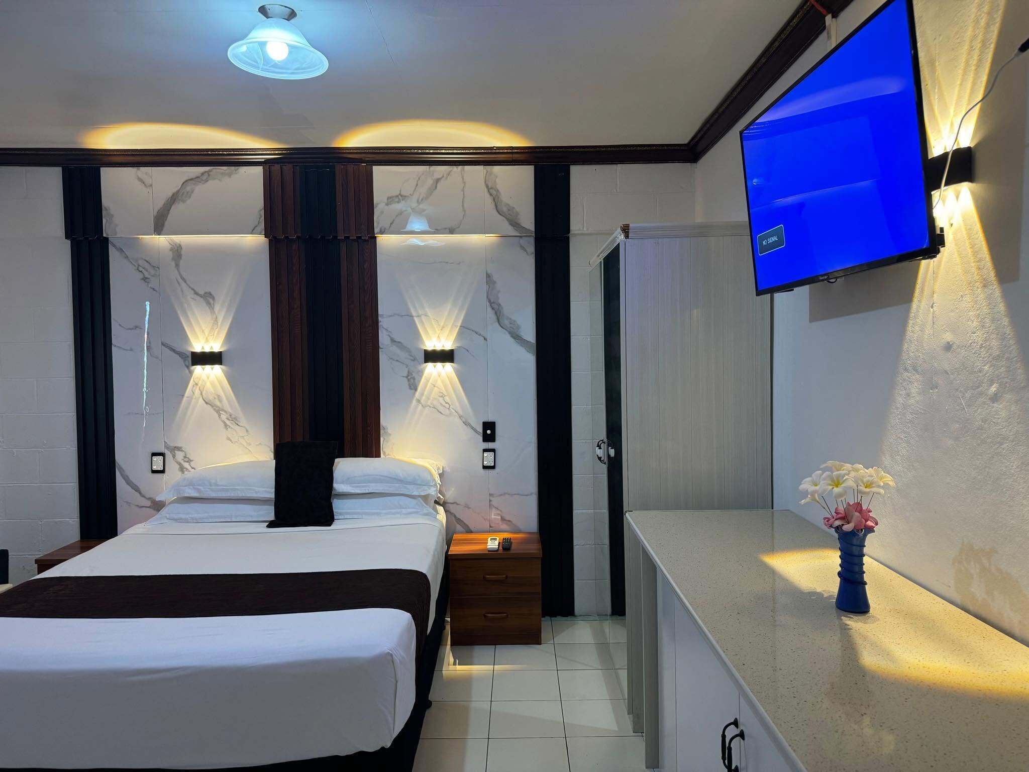 A hotel room with a bed, bedside table, nightstand, wall-mounted TV, and a vase with flowers.
