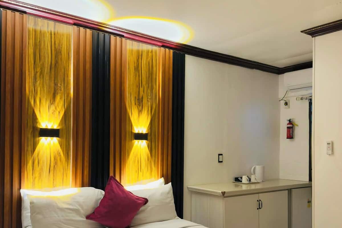 A hotel room with a large bed, a bedside table, a small kitchenette, and a mirror.