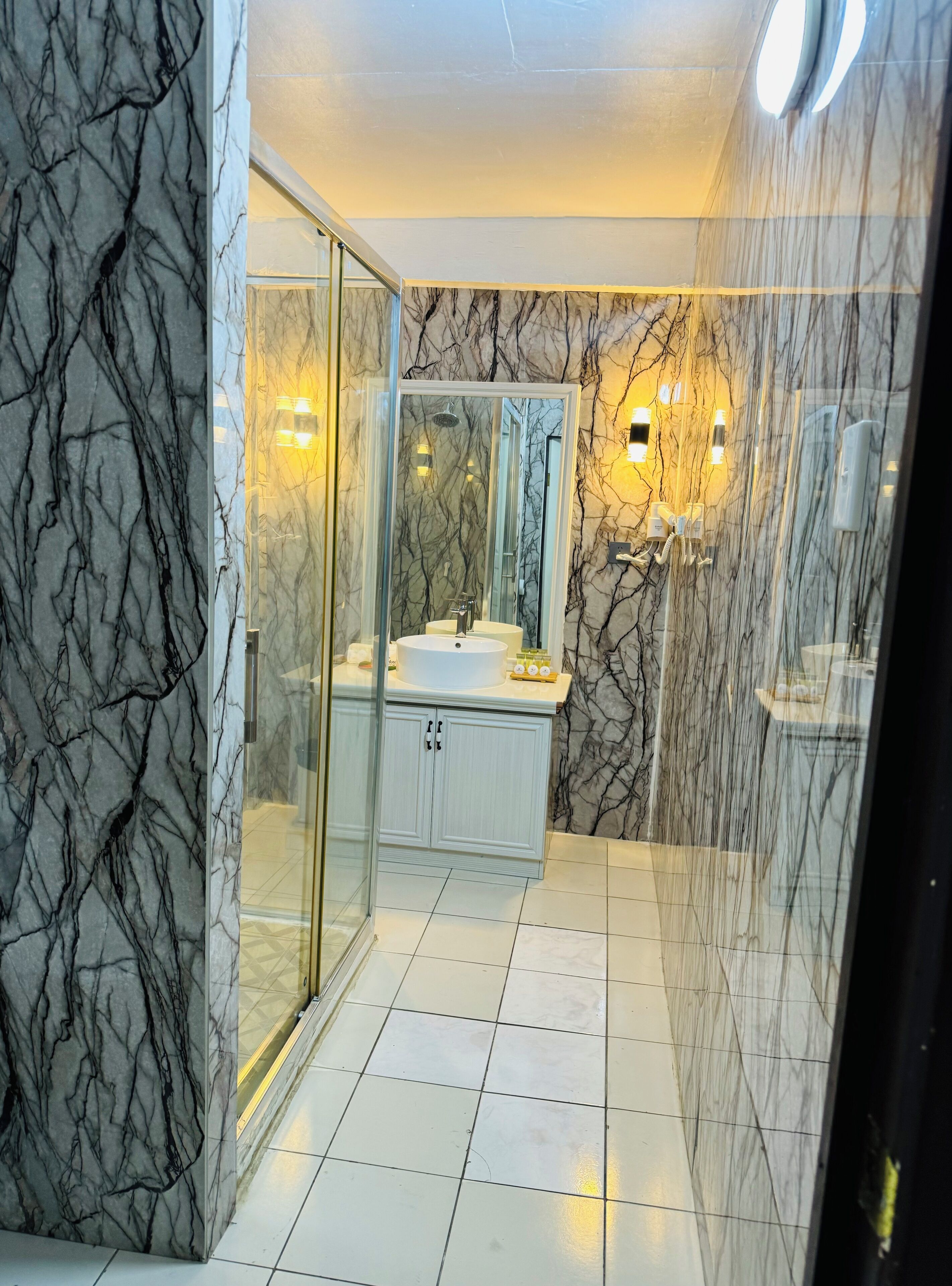 A modern bathroom with marble walls, a glass shower enclosure, and a white sink.