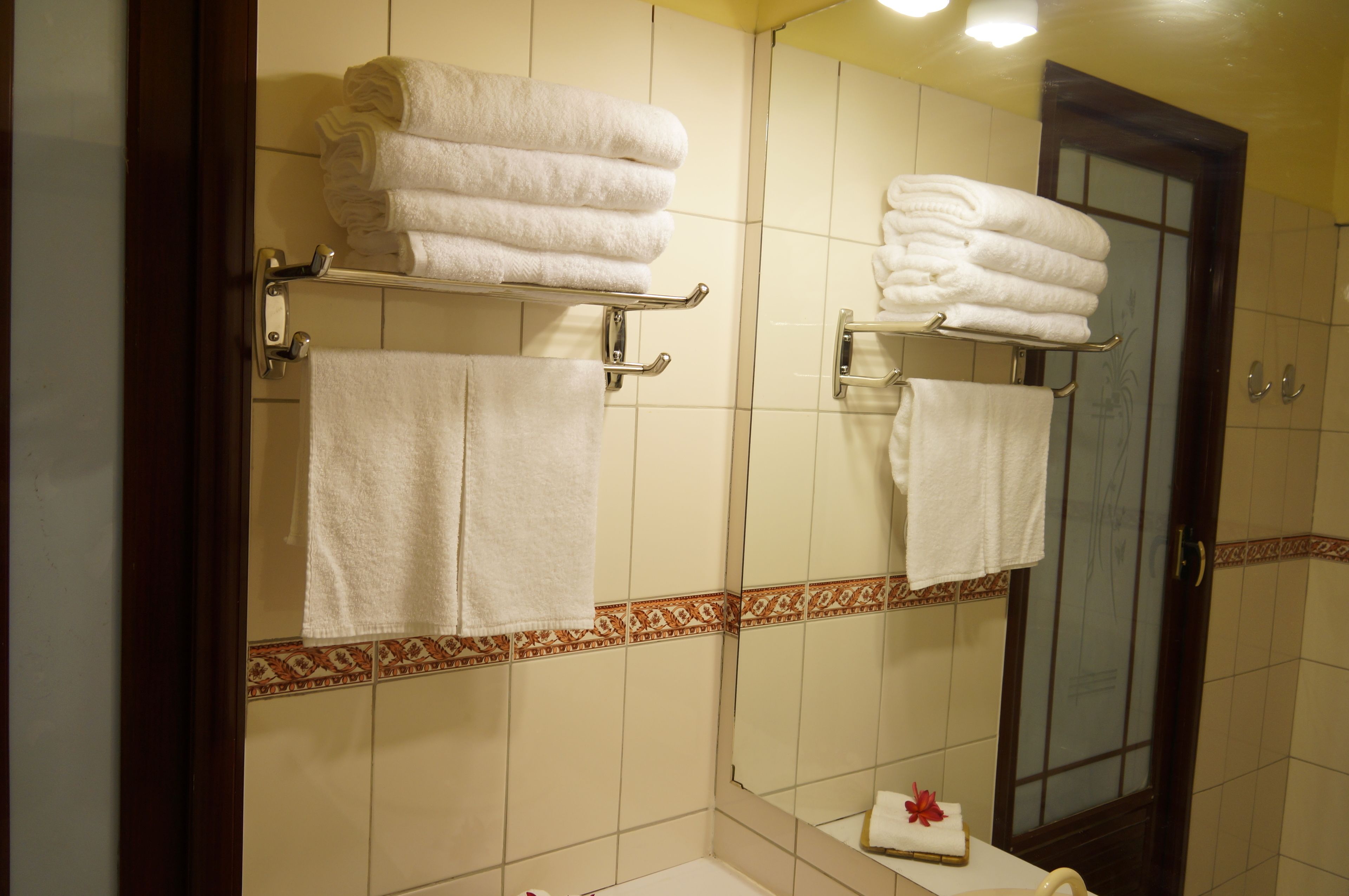 Ein Badezimmer mit zwei Handtuchhaltern, ordentlich gefalteten Handtüchern, einem Spiegel und einer dekorativen Fliesenleiste.