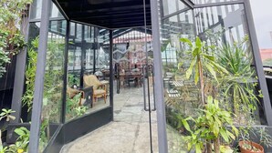Une véranda aux murs de verre, agrémentée de plantes d’intérieur et dotée d’un coin repas avec des chaises et des tables.